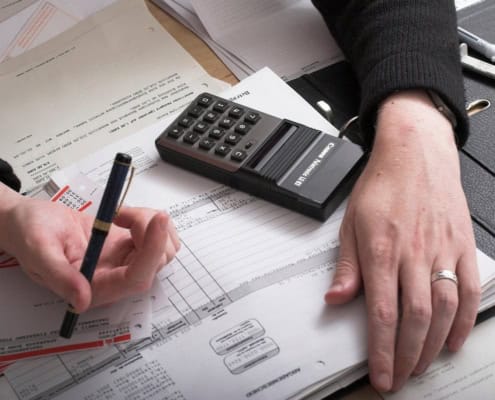 Datailaufnahme von zwei Händen auf Akten und einem Taschenrechner.