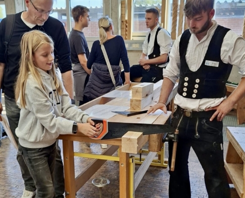 Berufemarkt2026_Zimmerer Ein Mädchen sägt einen Balken in der Zimmerei vom ÜAZ beim 26. Berufemarkt Westbrandenburg durch